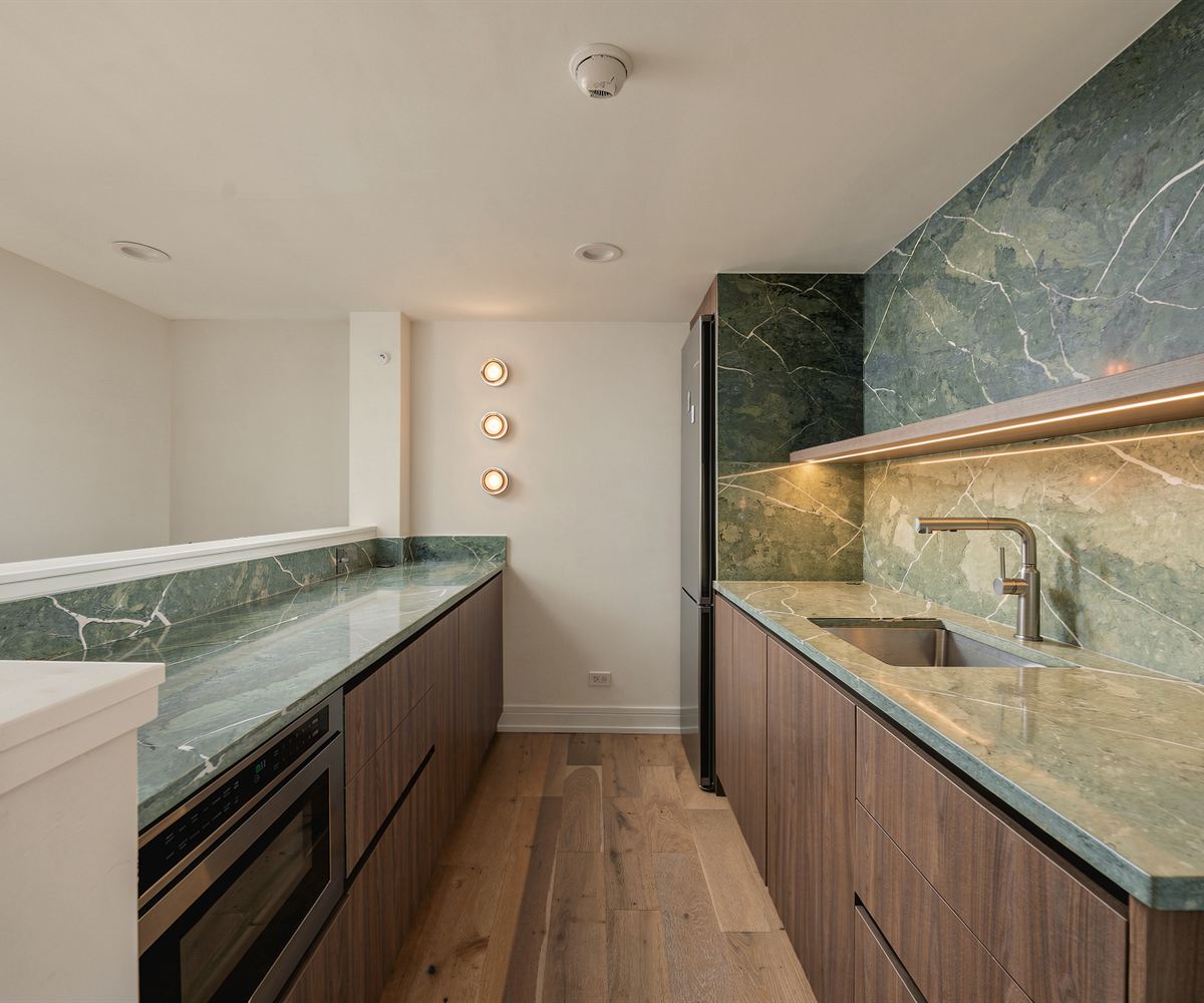 The same wall after: green marble wet bar with walnut cabinetry and an integrated lit shelf