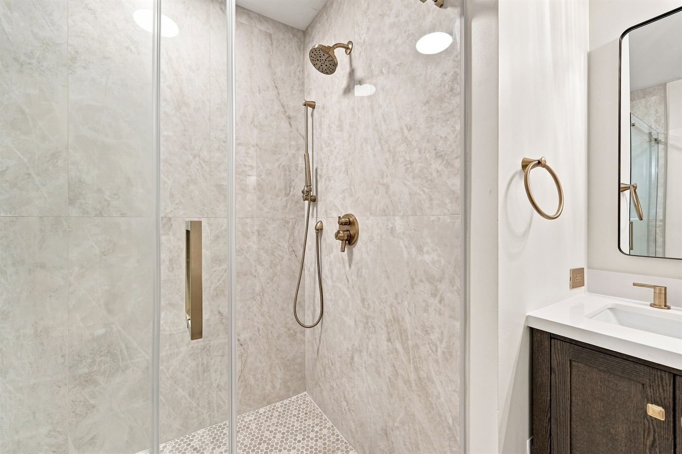 Marble-tiled walk-in shower with a glass enclosure, rain head and brass fittings